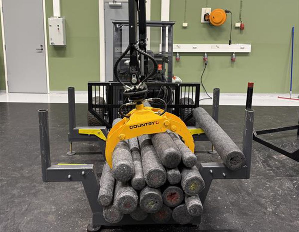 The miniature log-loading machine with its yellow grapple holding a bundle of training logs